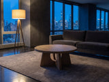 Fiesole Cerused Oak Veneer Round Pedestal Coffee Table seen from the side, on a wool rug in front of a velvet sofa in a city penthouse at blue hour
