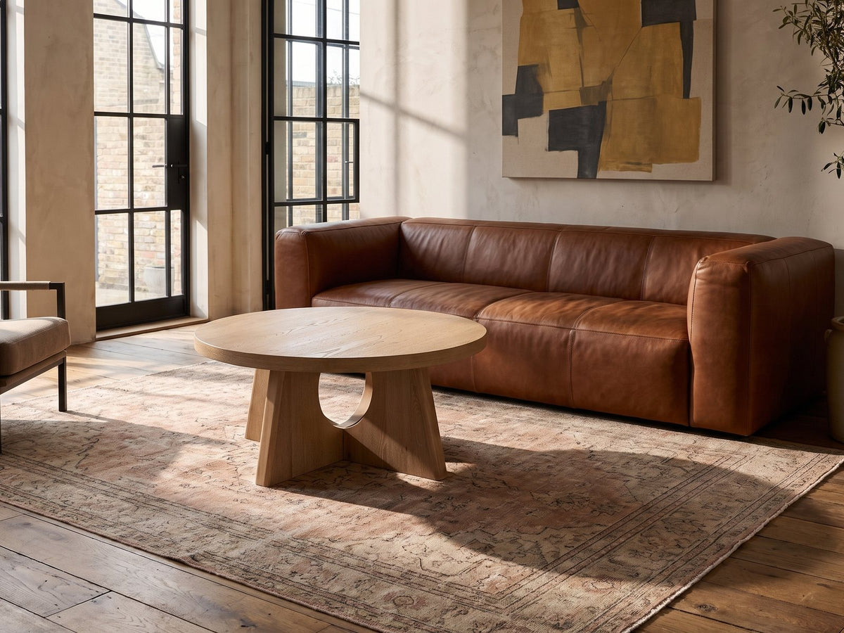 Fiesole Cerused Oak Veneer Round Pedestal Coffee Table on a vintage rug in front of a leather sofa in an industrial loft