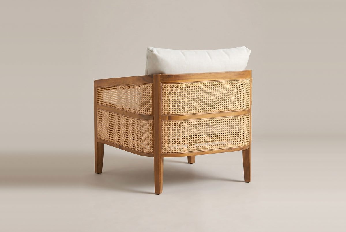 A Filicudi club armchair from behind: the curved acacia frame, two bands of woven rattan, square tapered legs and the back pillow above the frame