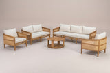 The three-seat Filicudi sofa and the round coffee table in a studio line-up with the club armchairs and loveseat: acacia frame, rattan arm panels and three ivory back pillows