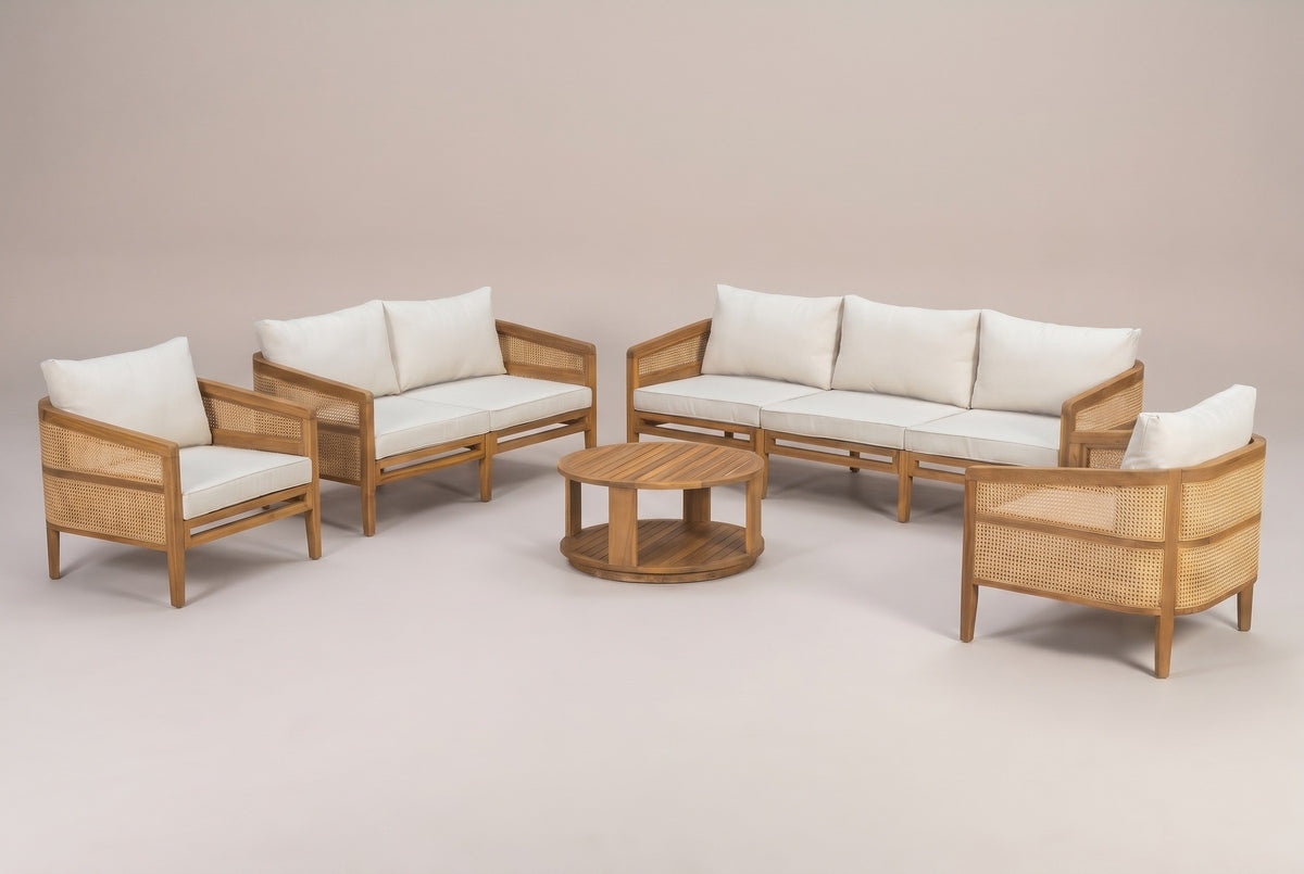 The three-seat Filicudi sofa and the round coffee table in a studio line-up with the club armchairs and loveseat: acacia frame, rattan arm panels and three ivory back pillows