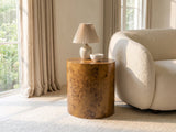 Fiumefreddo Walnut Burl Oval Pillar Side Table with a lamp and a ceramic bowl beside a cream boucle armchair in a bright plaster room