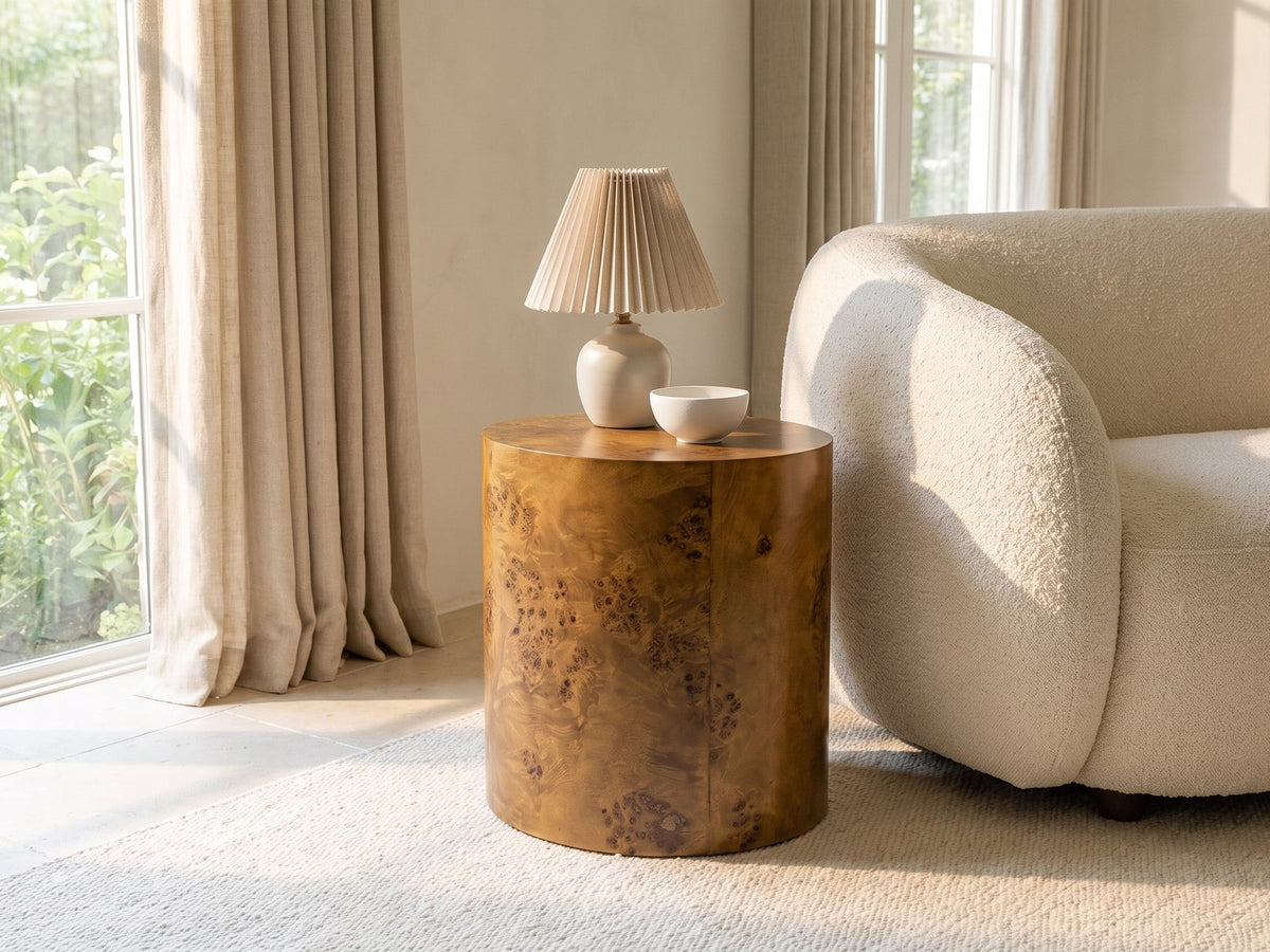 Fiumefreddo Walnut Burl Oval Pillar Side Table with a lamp and a ceramic bowl beside a cream boucle armchair in a bright plaster room