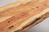 Close-up of the solid acacia top of the Foligno bench: honey and amber grain with small knots, board joints and a dark bark-coloured groove along the live edge