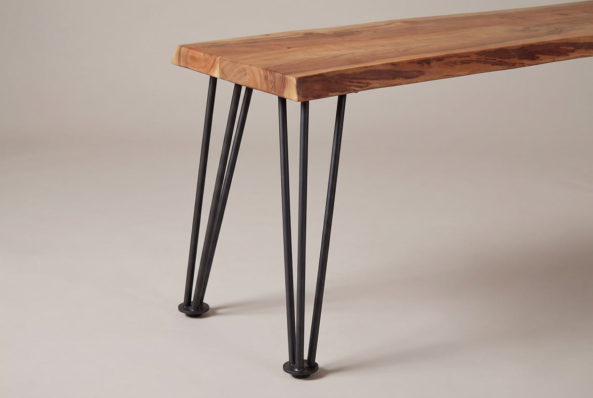Two Foligno hairpin legs at one end of the bench, each of three gunmetal iron rods meeting at a round disc foot under the acacia top