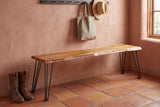 Foligno live-edge bench against a terracotta-pink lime-plaster wall in a Santa Fe entry hall with a saltillo tile floor, a coat rail with a tote and a straw hat, and leather boots beside it