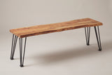 The Foligno bench in natural acacia, three-quarter view on a light studio backdrop