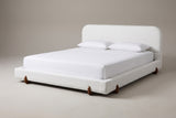 The Fossacesia bed in white textured fabric with walnut-tone rubberwood feet, a white mattress and pillows (not included), three-quarter view on a light studio backdrop