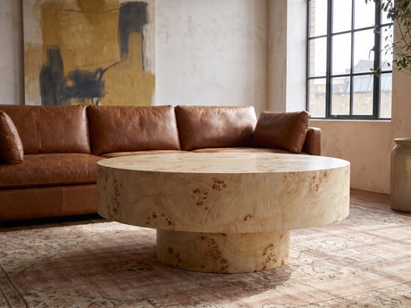 Fossano 31.5-Inch Round Burl Wood Veneer Pedestal Coffee Table seen from the side, on a vintage rug in front of a leather sofa in an industrial loft