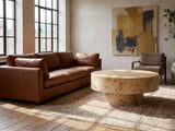 Fossano 31.5-Inch Round Burl Wood Veneer Pedestal Coffee Table on a vintage rug in front of a leather sofa in an industrial loft