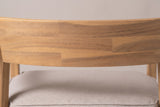Close-up of the curved acacia back panel on the Furnari club chair, joined strips in pale honey tones above the beige seat cushion