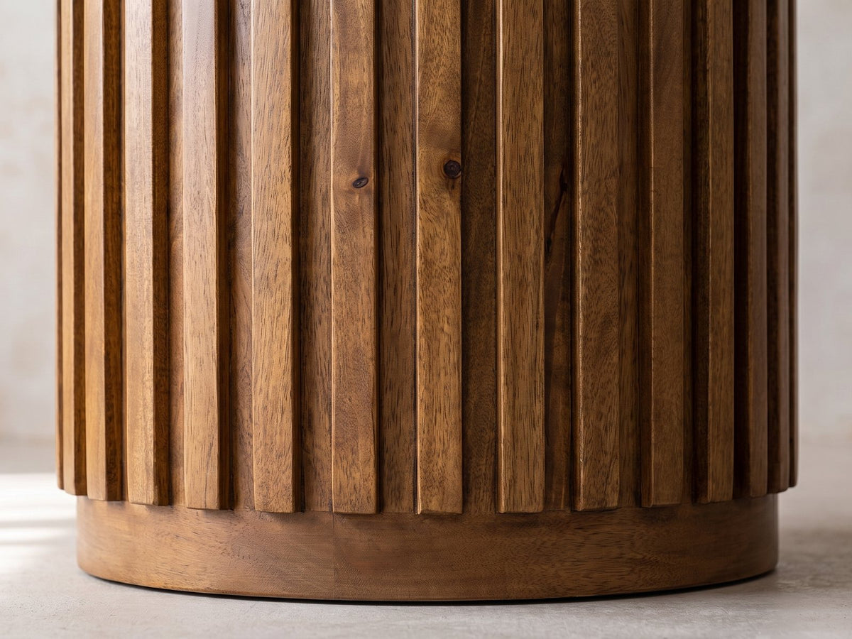 Close-up of the Fuscaldo 47-Inch Round Mango Wood Slatted Pedestal Dining Table: flat mango slats around the drum pedestal above its plain plinth ring