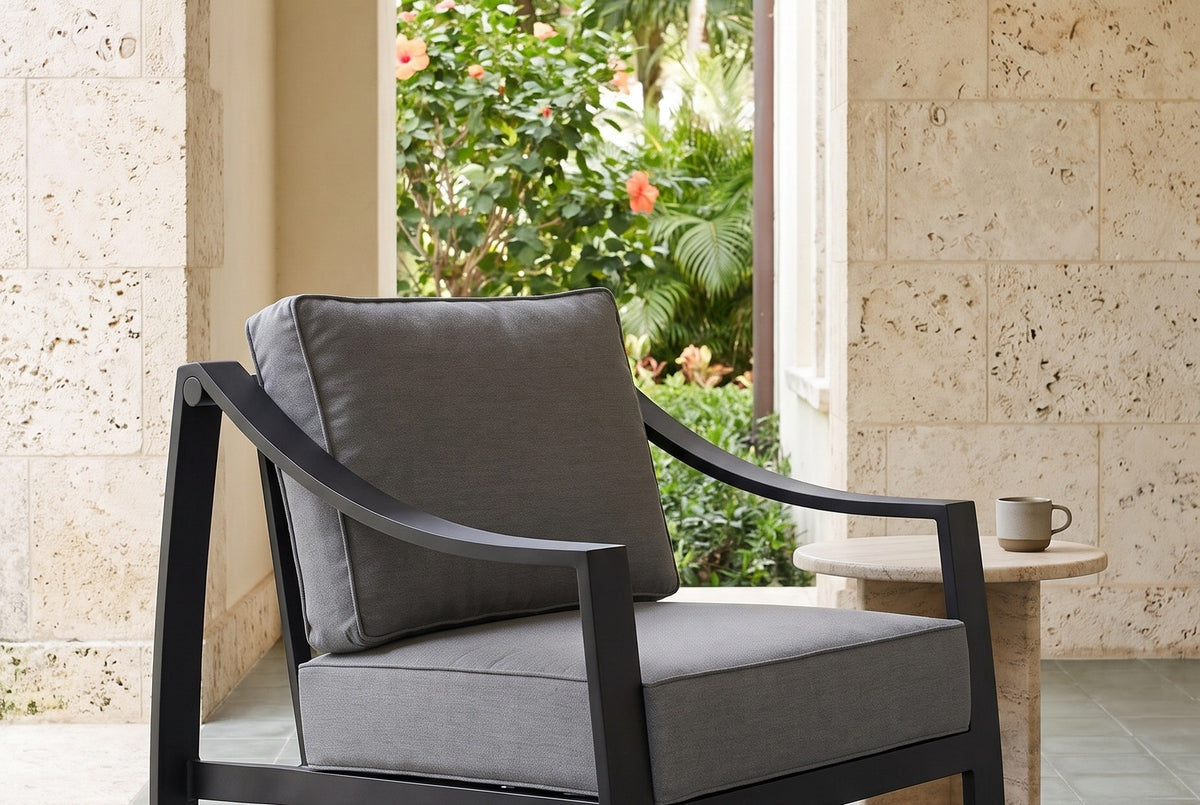 Galati black aluminum lounge chair in a Coral Gables loggia with coral stone walls, gray-green cement tiles and an arch onto a garden of palms and hibiscus (side table not included)