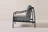 The Galati lounge chair seen from the side: the curved arm rising from the front leg to the round cap on the rear leg, the bowed rear leg and the side rail