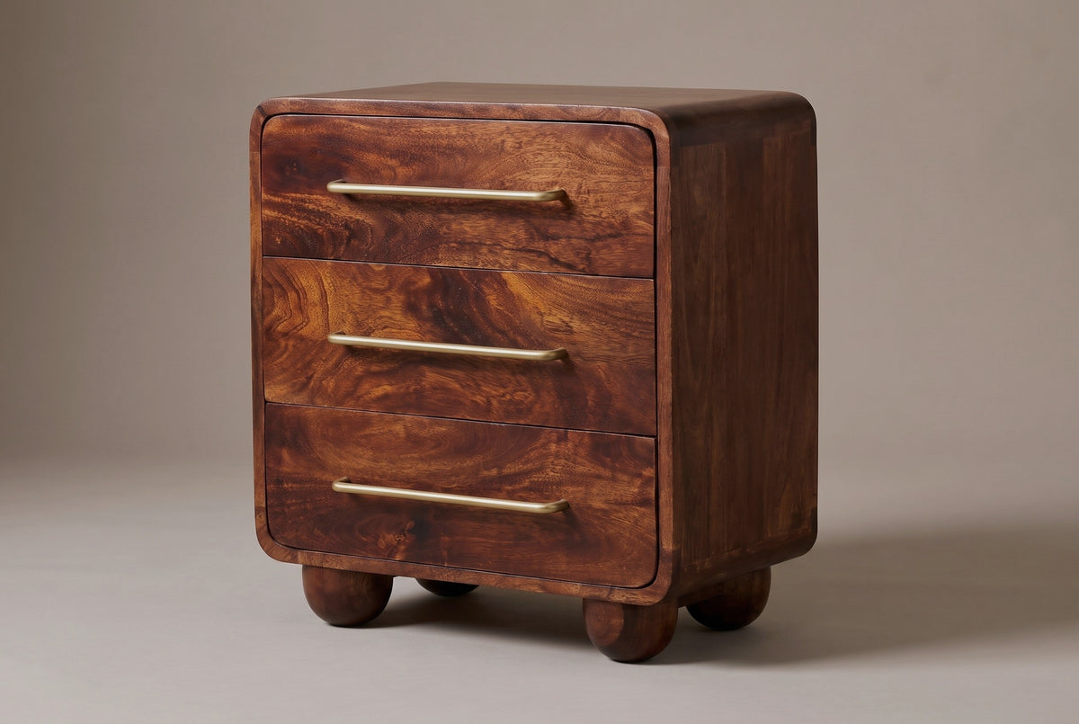 The Galtelli three-drawer nightstand in chestnut mango with long brass bar pulls, rounded corners and four ball feet, three-quarter view on a light studio backdrop