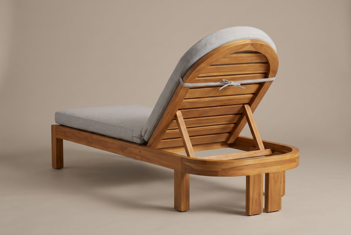 A Gangi chaise from behind: the arched slatted backrest raised on its prop, the curved acacia band and the two flat legs at the head end