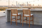 Two Ganzirri acacia bar stools with light brown woven backs tucked at a board-formed concrete bar on an Austin rooftop terrace at golden hour, string lights and the skyline behind (bar counter not included)