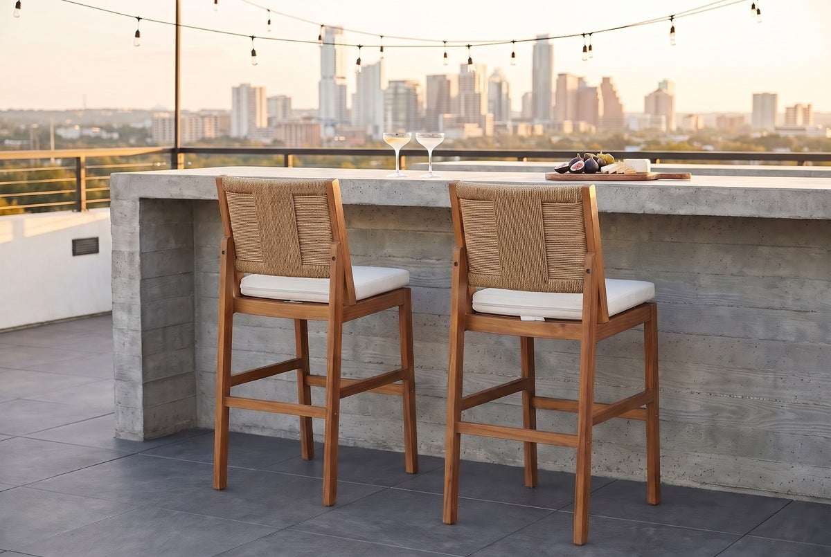 Two Ganzirri acacia bar stools with light brown woven backs tucked at a board-formed concrete bar on an Austin rooftop terrace at golden hour, string lights and the skyline behind (bar counter not included)