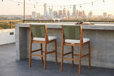 Two Ganzirri acacia bar stools tucked at a board-formed concrete bar on an Austin rooftop terrace at golden hour, string lights and the skyline behind (bar counter not included)