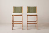 The two Ganzirri bar stools seen straight from the front: woven backs, ivory cushions, square legs and the low footrest rails