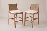 The two Ganzirri acacia bar stools with light brown woven backs and ivory cushions, three-quarter view on a light studio backdrop