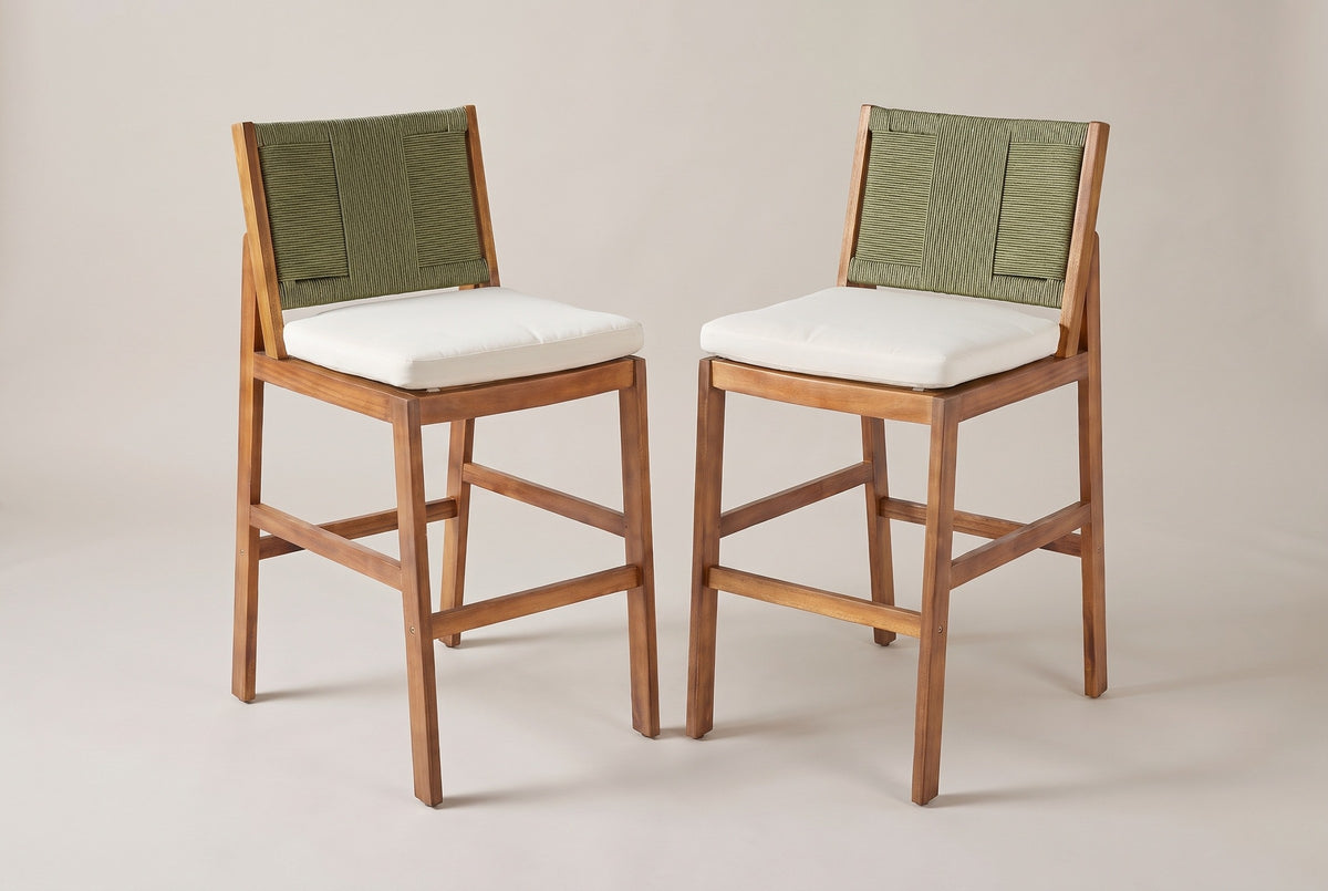 The two Ganzirri acacia bar stools with sage-green woven backs and ivory cushions, three-quarter view on a light studio backdrop