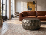 Gavi 32-Inch Round Antique Bronze Faceted Aluminum Drum Coffee Table on a vintage rug in front of a leather sofa in an industrial loft
