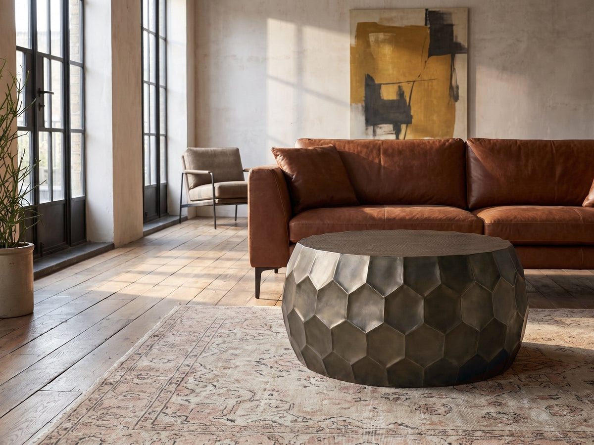 Gavi 32-Inch Round Antique Bronze Faceted Aluminum Drum Coffee Table on a vintage rug in front of a leather sofa in an industrial loft
