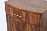 The upper front of the Gavoi nightstand: the curved top edge, the reeded drawer with its brass bar pull, and the top of a reeded door