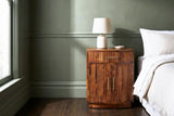 Gavoi fluted mango bow-front nightstand with a ceramic lamp beside a bed in a San Francisco bedroom with a sage green plaster wall and dark oak floorboards