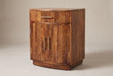The Gavoi nightstand in mocha mango with a bowed front, one reeded drawer with a brass bar pull and two reeded doors with vertical brass pulls, three-quarter view on a light studio backdrop