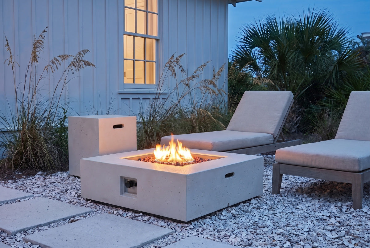 Gela fire pit and tank holder in white concrete, lit on crushed oyster shell beside a white board-and-batten cottage in Seaside, Florida at blue hour (chaise lounges not included)