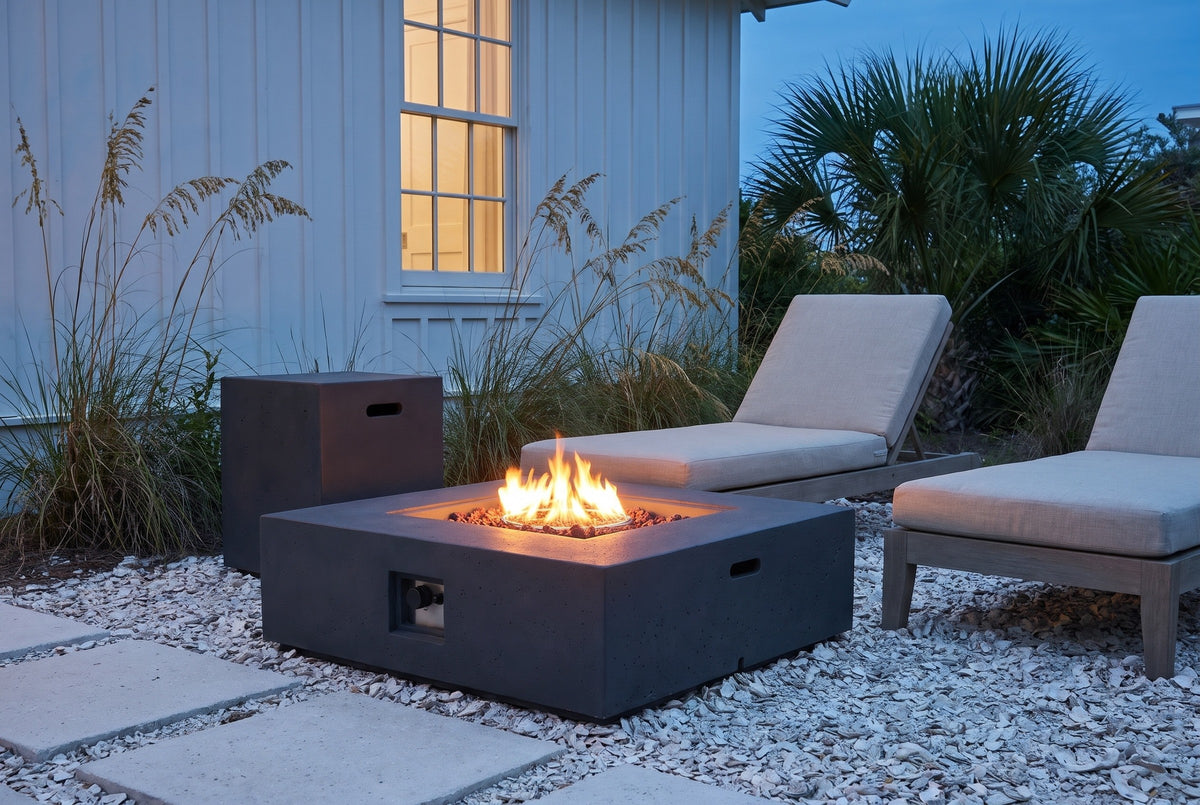 Gela fire pit lit on crushed oyster shell beside a white board-and-batten cottage in Seaside, Florida at blue hour, the tank holder behind it (chaise lounges not included)
