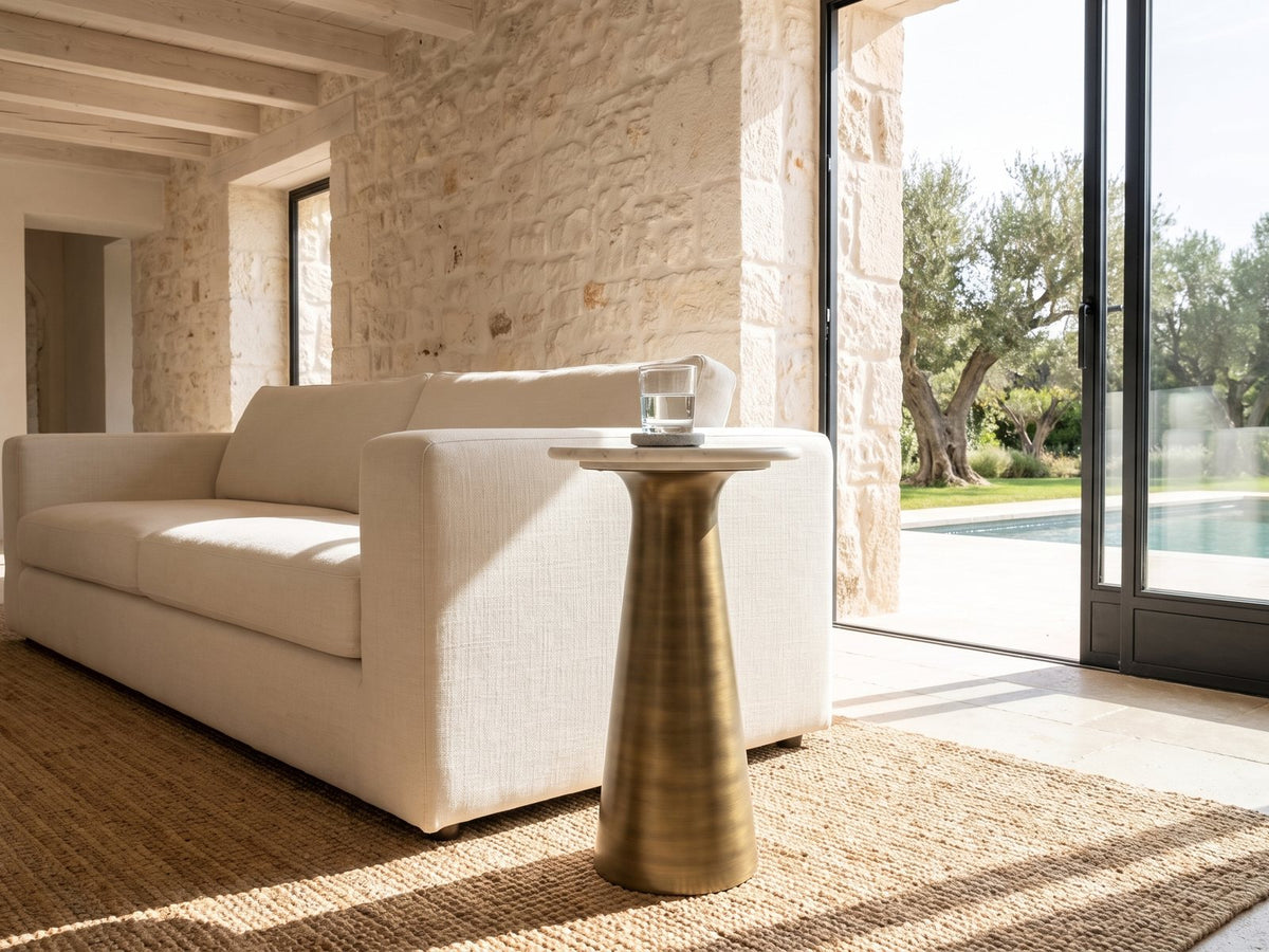 Genazzano White Marble Tapered Pedestal Side Table beside a linen sofa in a poolside villa