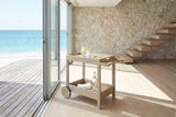 Gerocarne 36-Inch Acacia Wood Outdoor Rolling Bar Cart in an oceanfront glass house