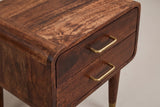 The front corner of the Ghilarza nightstand: the top rolling over a rounded corner of curved mango blocks, two flush drawers with their slim brass U-shaped pulls and the top of a tapered leg