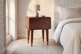 Ghilarza chestnut mango nightstand against a whitewashed brick wall in a Brooklyn bedroom with a herringbone floor and an arched window