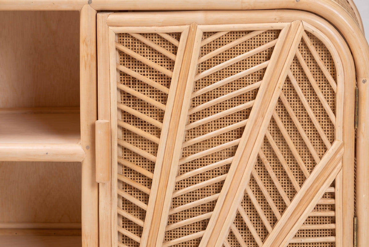 A door of the Giovinazzo sideboard up close: thick double rattan spines with thin rods branching off like palm veins, open cane between the rods, and the short round rattan pull on the inner edge