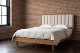 Giulianova wheat pine bed with an oatmeal scalloped headboard against a warm exposed brick wall in a Chicago loft bedroom, a tall black steel window at the left