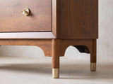 Close-up of the Grado 34-Inch Warm Walnut 5-Drawer Chest: a round walnut leg with a brass cap under an arched apron