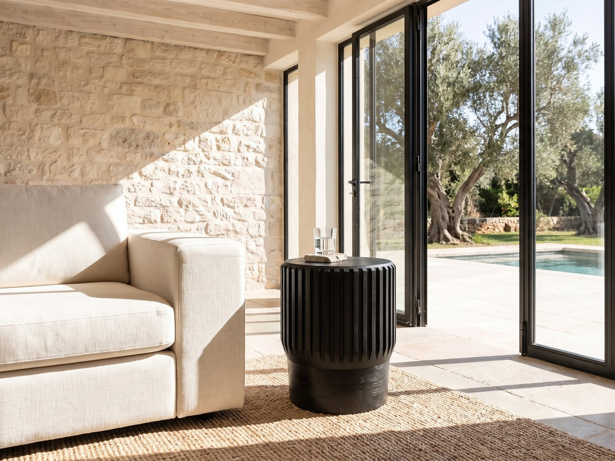 Grottole Black Mango Ribbed Drum Side Table beside a linen sofa in a poolside villa