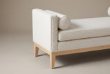One end of the Gualdo bench: the flat boucle track arm, a round bolster against it, the long seat cushion, the upholstered base and a tapered wooden leg