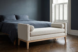Gualdo ivory boucle bench at the foot of a bed with slate-blue linen bedding in a Brooklyn brownstone bedroom with a deep blue wall and a dark herringbone floor (bed not included)