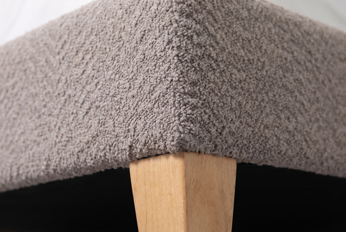 Close-up of the Guardiagrele bed where the taupe gray boucle base meets a tapered natural wood leg