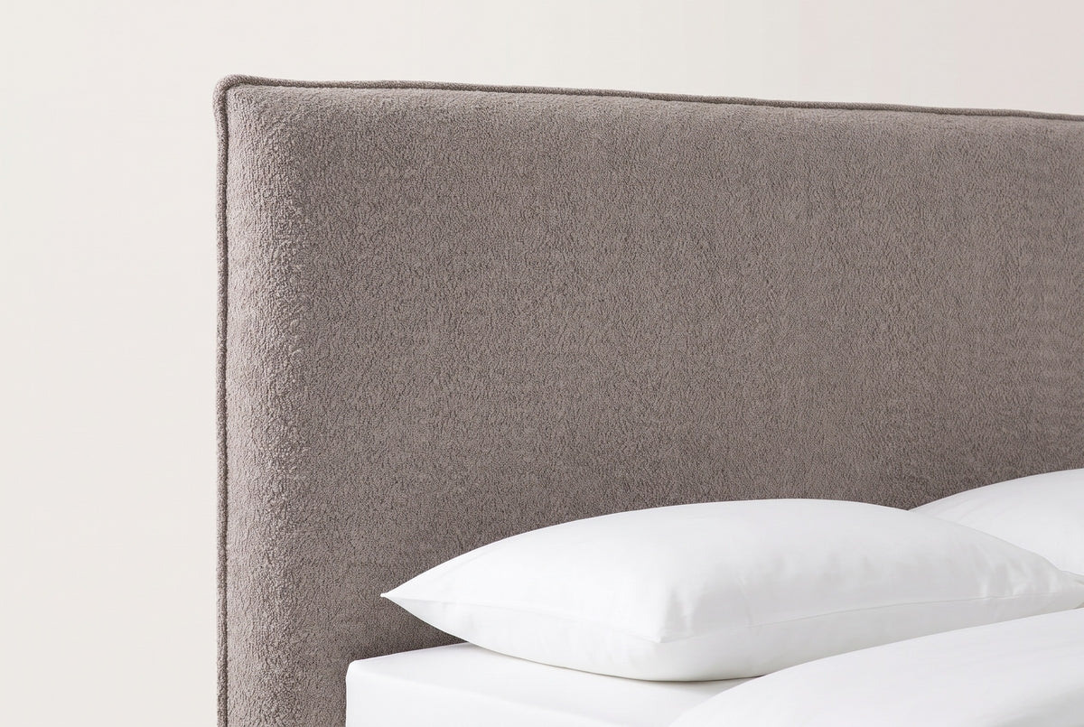 The top corner of the Guardiagrele headboard: a flat taupe boucle panel with a thin flat welt, above a white pillow