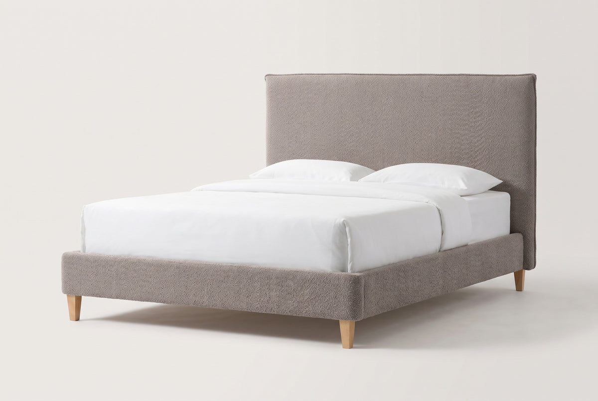 The Guardiagrele bed in taupe gray boucle with a white mattress and pillows (not included), three-quarter view on a light studio backdrop