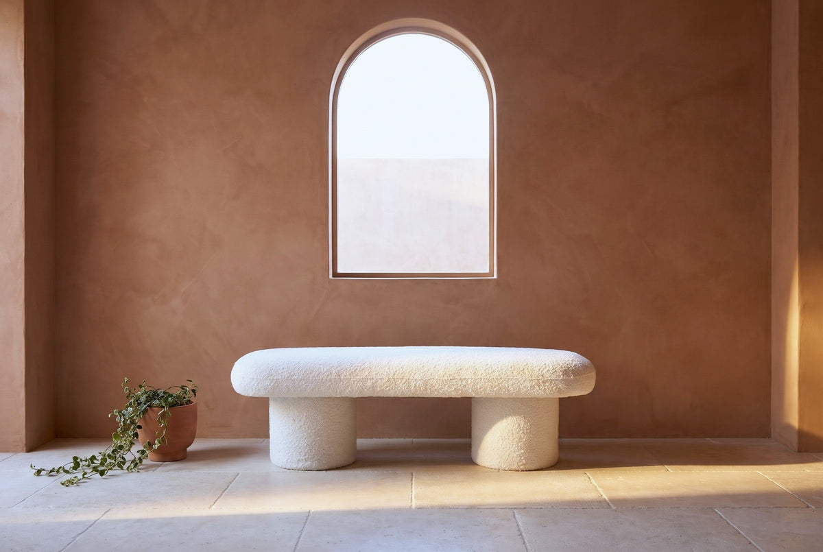 Gubbio ivory boucle bench under an arched window in a Lisbon living room with a terracotta lime-plaster wall and a pale limestone floor