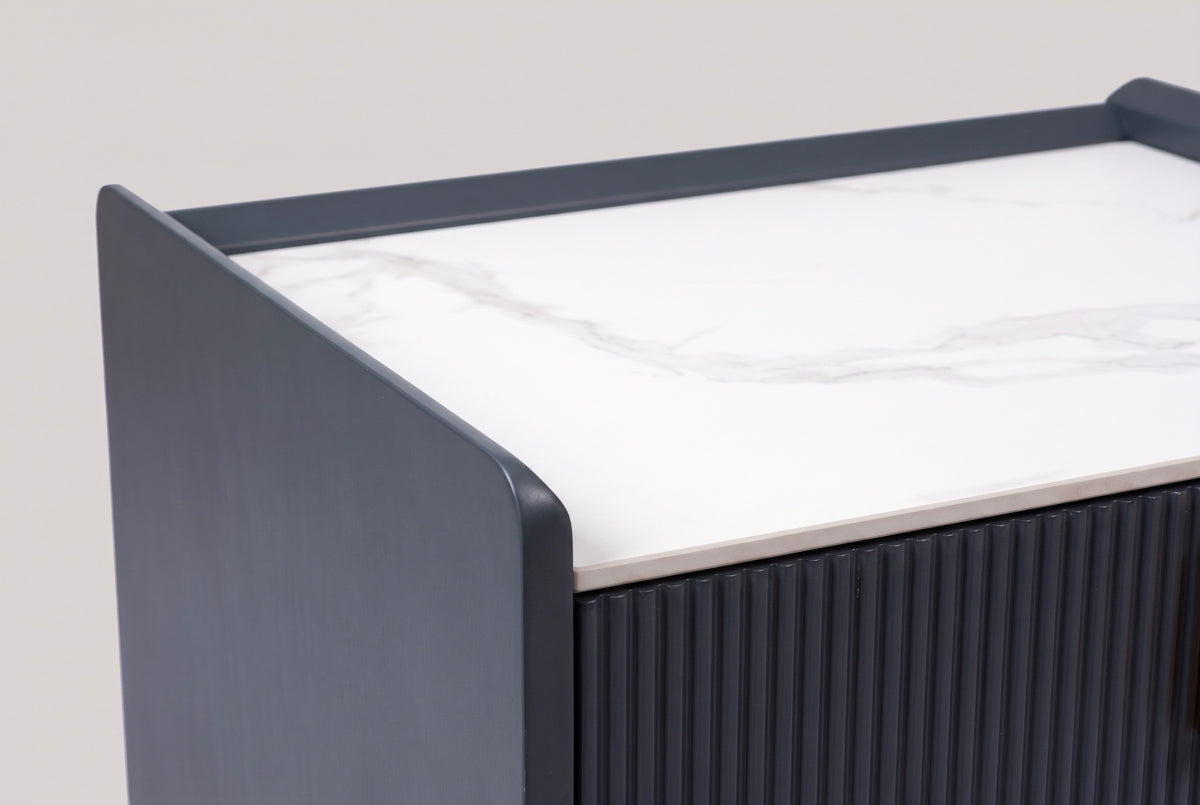 The top of the Guspini nightstand: white sintered stone with gray veins, a charcoal side panel rising above it and the reeded drawer front below