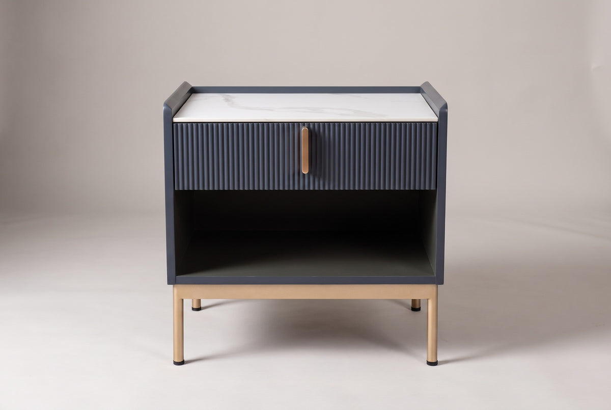The Guspini nightstand, front view on a light studio backdrop: white stone top, reeded drawer with a gold-tone pull, open cubby and four gold-tone legs