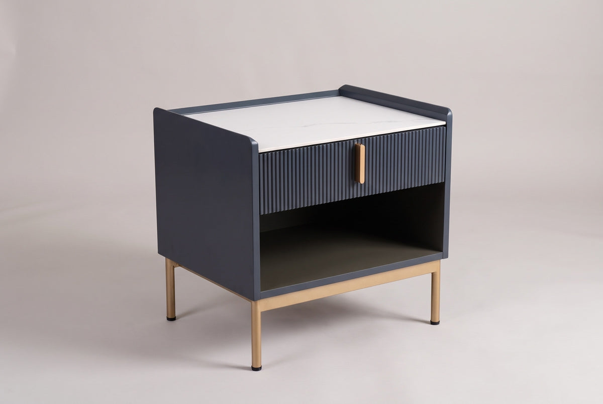 The Guspini nightstand with a white sintered stone top, reeded charcoal drawer, open cubby and gold-tone legs, three-quarter view on a light studio backdrop